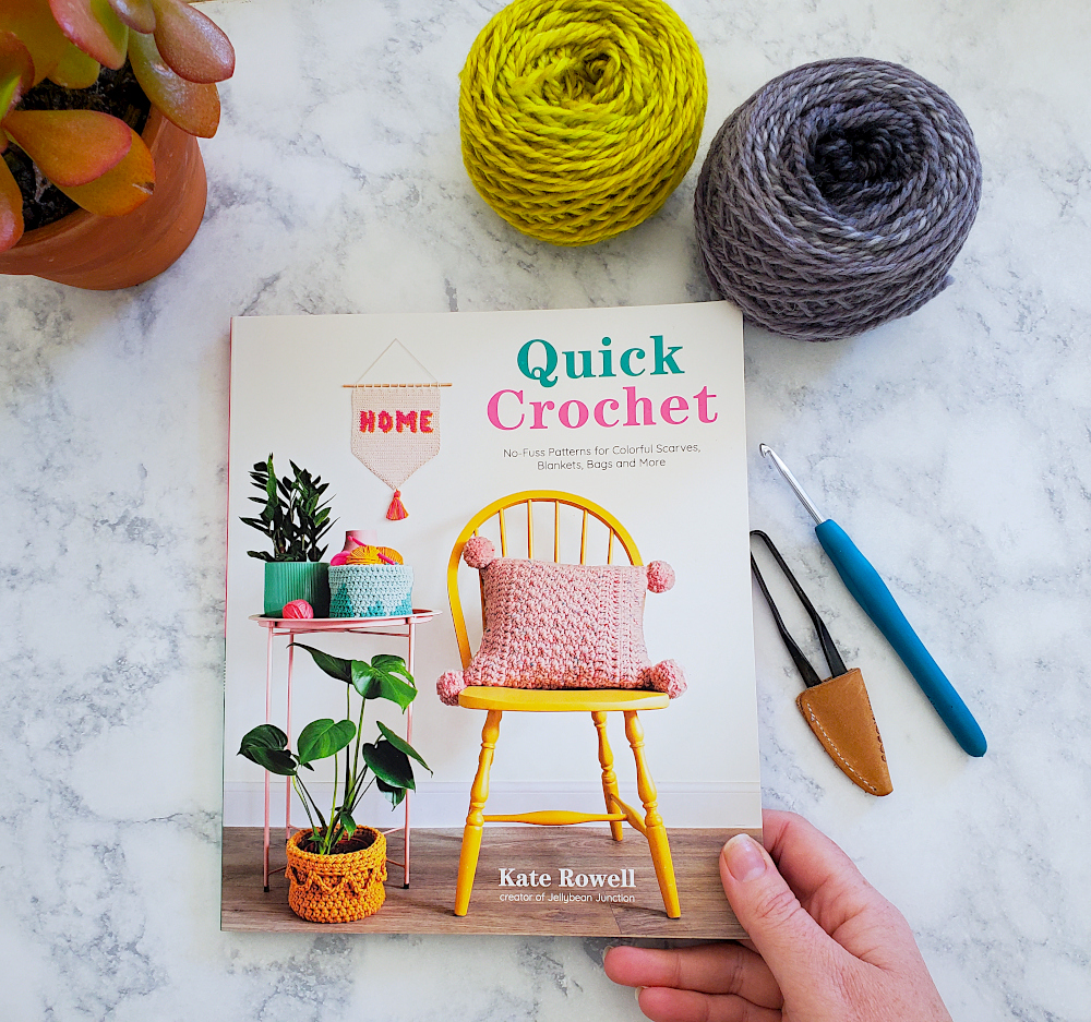[Image description] Top down view of a white woman's hand holding a copy of Quick Crochet