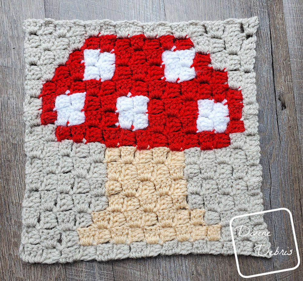 [Image description] C2C Mushroom Afghan Square laying in the center of the frame on a wood-grain background. 