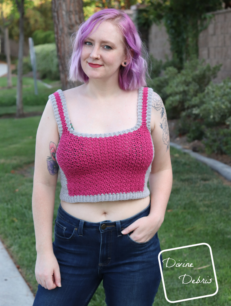 [Image description] A white woman with purple hair stands with one hand in her pocket in front of a green landscape in the pink and gray Kelsey Tank Top