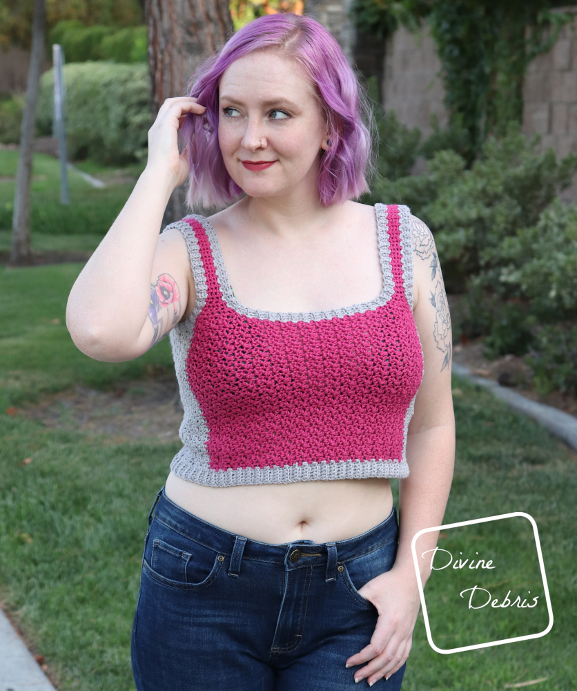 [Image description] A white woman with purple hair plays with her hair looking to her right in front of a green landscape in the pink and gray Kelsey Tank Top