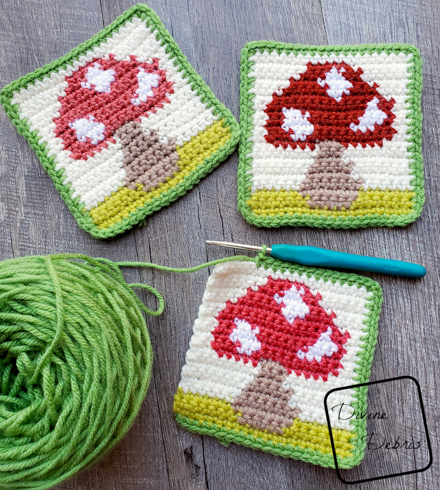 [Image description] Top down view of three Cute Mushroom Coasters, one unfinished on the bottom of the frame, attached to the cake of yarn.