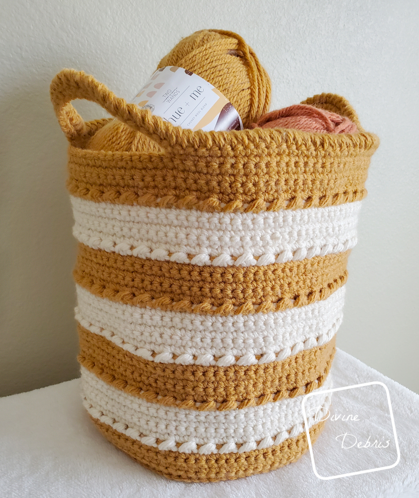 [Image description] Yellow and white striped Claire Basket sits on white fuzzy blanket against a cream background.